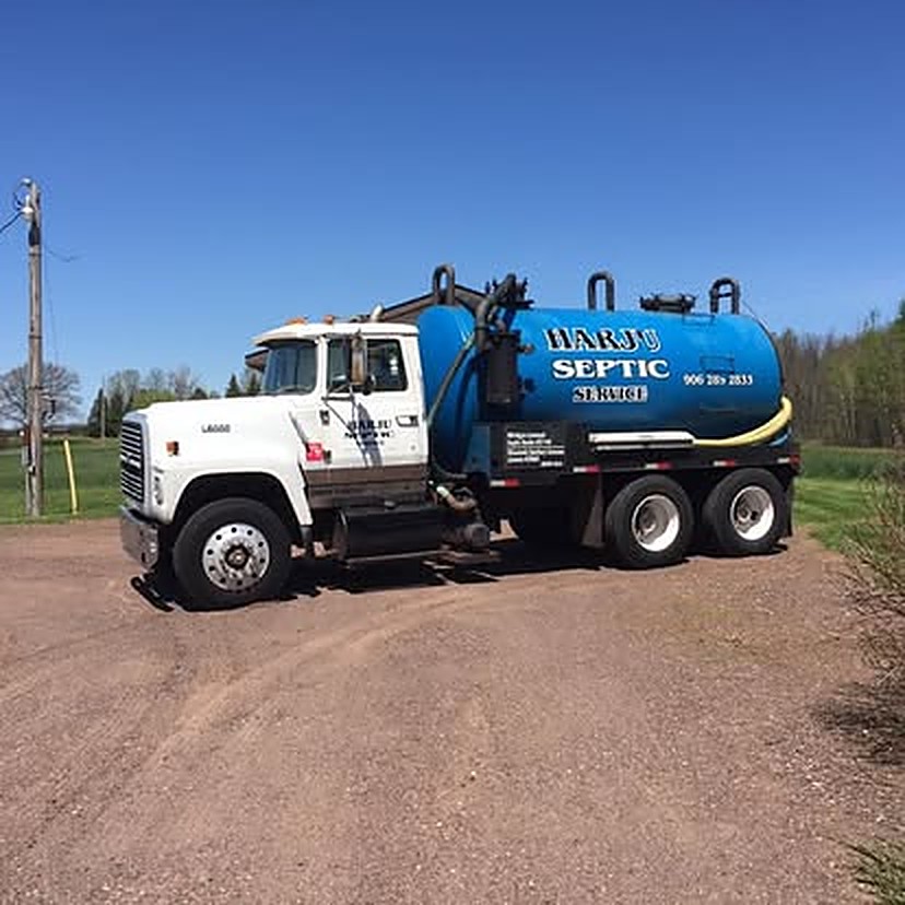 Harju Septic Service tank truck — HARJU SEPTIC and (906) 285-2833 painted on the blue tank — on a gravel road in the western U.P.