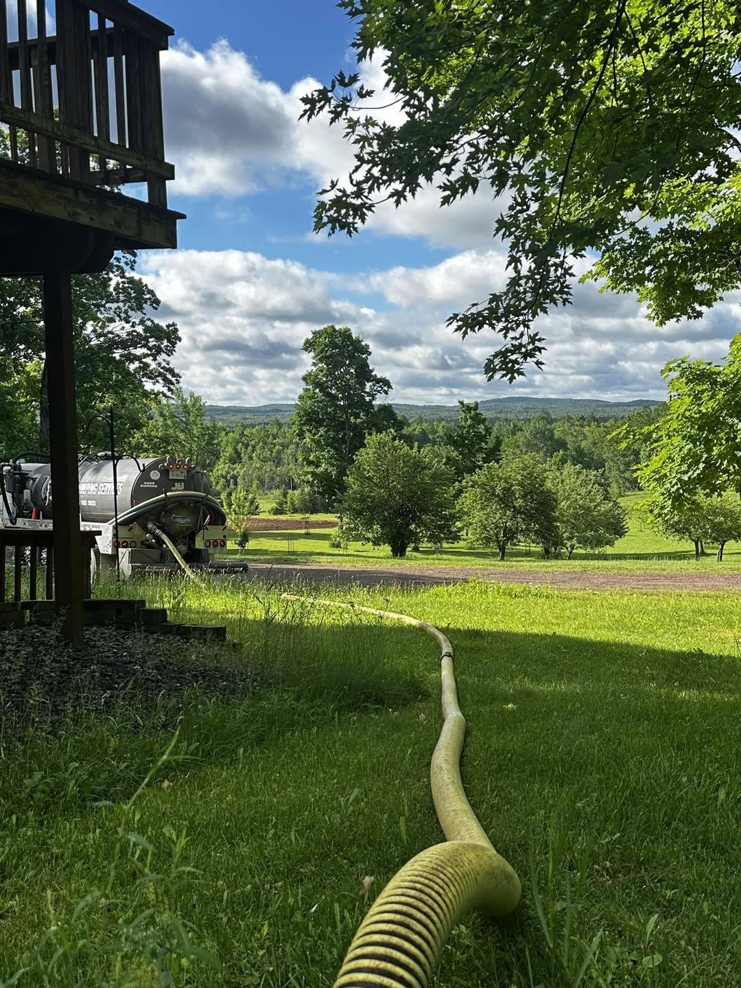 Pump hose running across a cabin lawn to the Harju truck, with the western U.P. hills beyond