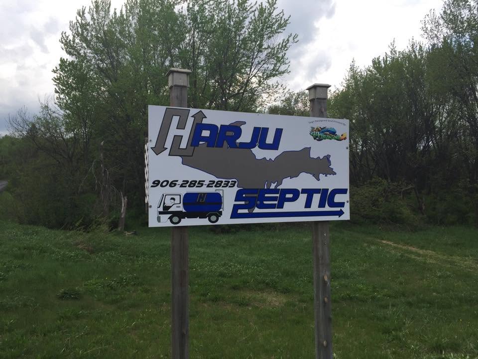 The hand-painted Harju Septic road sign on the county road — blue lettering with a gray Upper Peninsula map